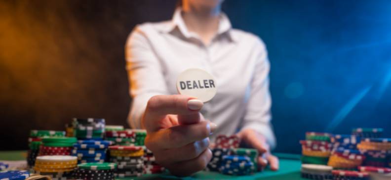 Dealerknappen hålls upp vid ett pokerbord